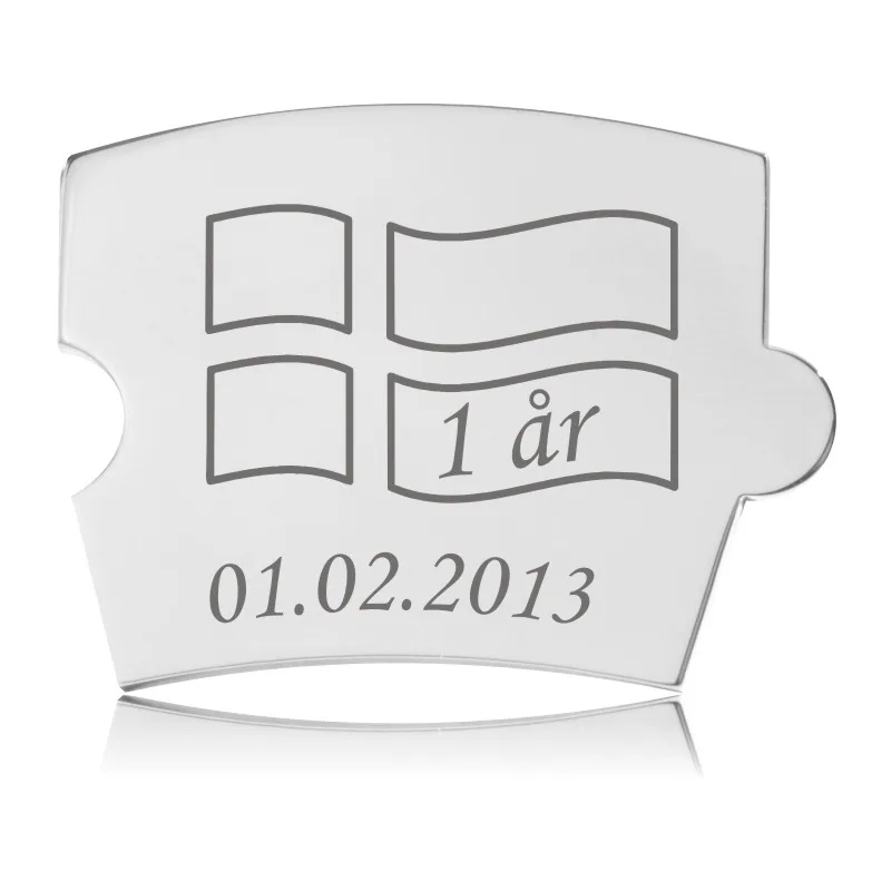 Sølvfarvet Memozz Spin brik i bølget flag-form med graveret design til fødselsdag. Teksten "1 år" er skrevet. Den er fremstillet i håndpoleret rustfrit stål.