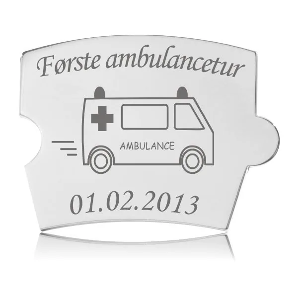 Memozz Spin brik i blankpoleret rustfrit stål med gravering af en ambulance og teksten "Første ambulancetur"