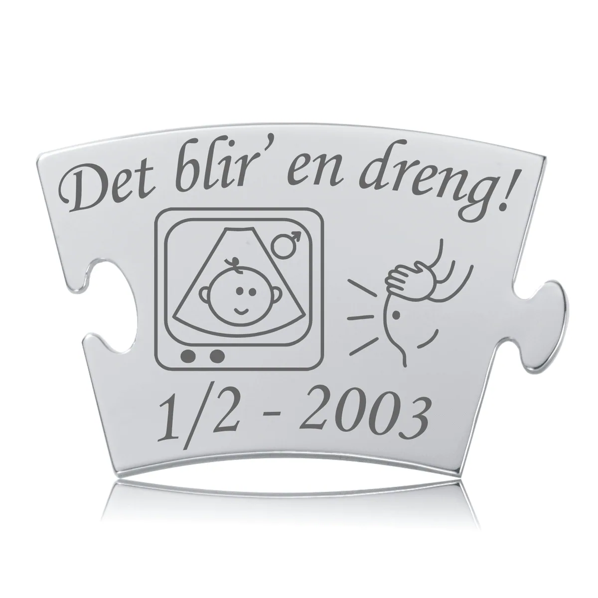 Rektangulær mindebrik i sølvfarvet rustfrit stål med teksten "Det blir' en dreng!" over et scanningsbillede af en baby og en gravid mave. Graveringen er mørk og står tydeligt frem på det polerede metal.