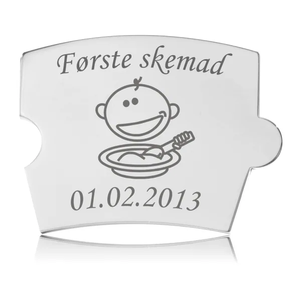 Memozz Spin mindebrik "Første skemad" i skinnende rustfrit stål, med en glad baby der spiser grød og teksten "Første skemad".