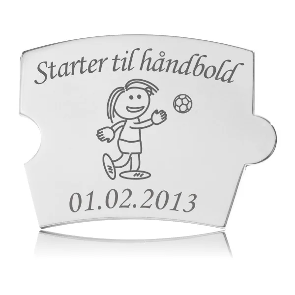 Memozz Spin brik i stål med gravering af pige der spiller håndbold og teksten 'Starter til håndbold'.