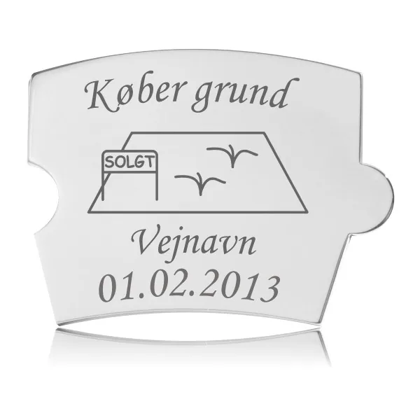 Memozz Spin mindebrik "Køber grund" i håndpoleret rustfrit stål med tydelig lasergravering af en grund, "SOLGT" skilt, vejnavn og dato.