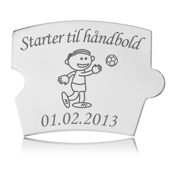 Memozz Spin brik i håndpoleret rustfrit stål, graveret med en tegning af en glad dreng der kaster en håndbold og teksten "Starter til håndbold"