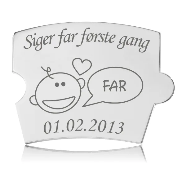 Memozz Spin brik i poleret rustfrit stål med teksten "Siger far første gang" og et tegnet ansigt med taleboble "FAR"