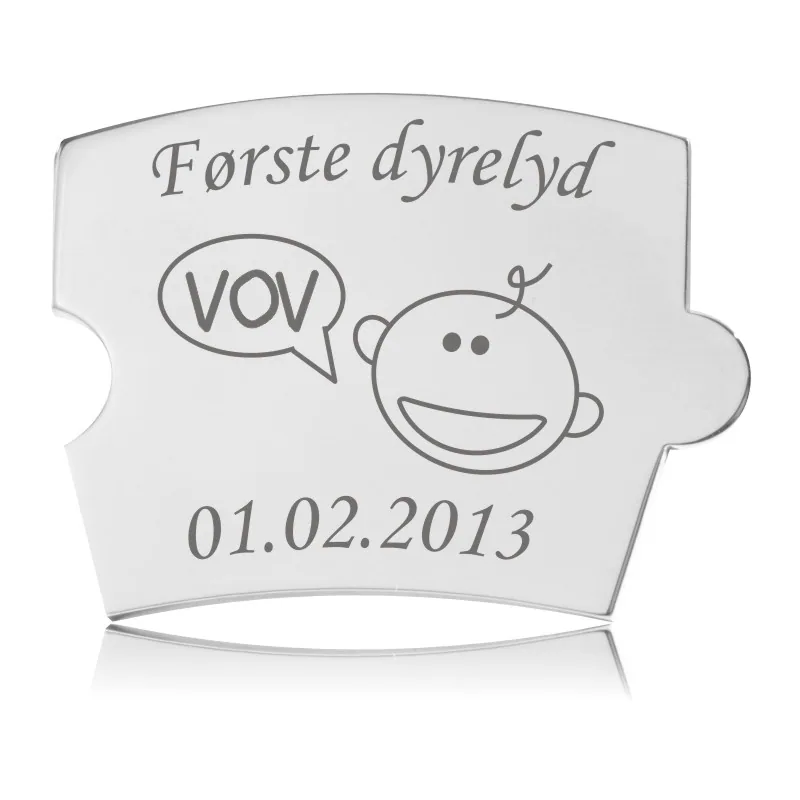 Memozz Spin brik i poleret stål med gravering af 'Første dyrelyd' og en tegning af et babyansigt, der siger 'VOV'.