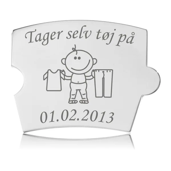 Memozz Spin mindebrik i håndpoleret rustfrit stål med gravering "Tager selv tøj på" og tegning af barn med tøj.