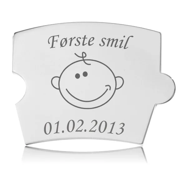 Memozz Spin brik i håndpoleret rustfrit stål med teksten "Første smil" og en tegning af et glad babyansigt