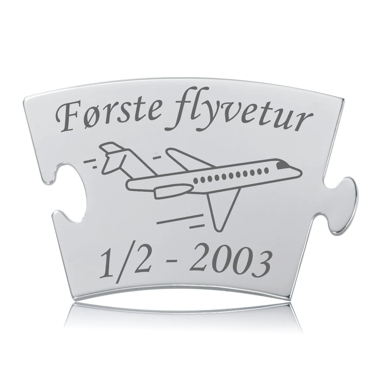 Blank, skinnende Memozz Classic brik med teksten "Første flyvetur" og et stregtegnet fly i mørkegrå gravering.