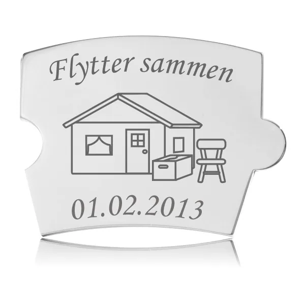 Memozz Spin brik i håndpoleret rustfrit stål med indgravering af hus, flyttekasse, stol og teksten "Flytter sammen". Den dybe mørkegrå gravering fremhæver designet.