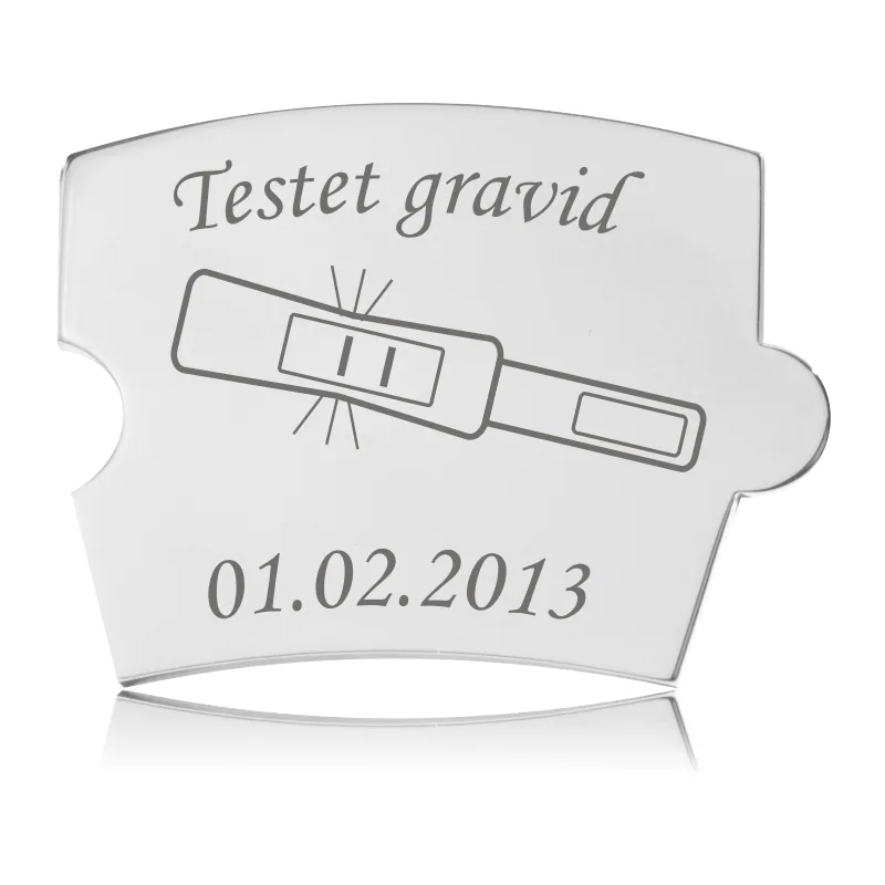 Memozz Spin brik "Testet Gravid" i håndpoleret rustfrit stål med gravering af graviditetstest og tekst.