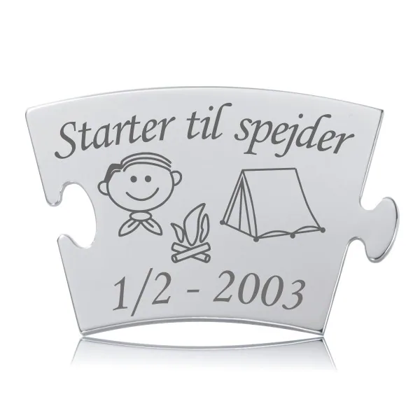 Memozz Classic brik foreviger en drengs spejderstart med indgraveret tekst, en dreng, lejrbål og telt illustration. Den blanke overflade reflekterer et varmt lys.