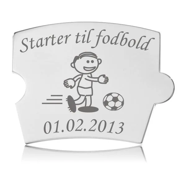 Memozz Spin brik i stål med gravering af dreng der starter til fodbold, vist på hvid baggrund.