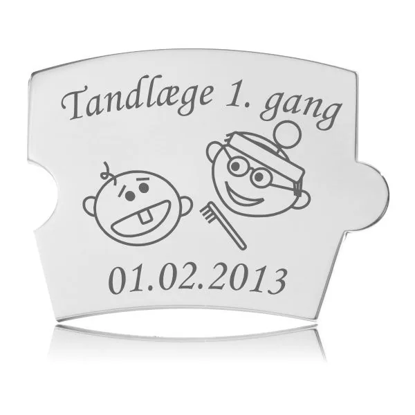 Memozz Spin brik i poleret rustfrit stål med gravering af en baby med én tand og en tandlæge med tandbørste, tekst "Tandlæge 1. gang" og plads til dato.