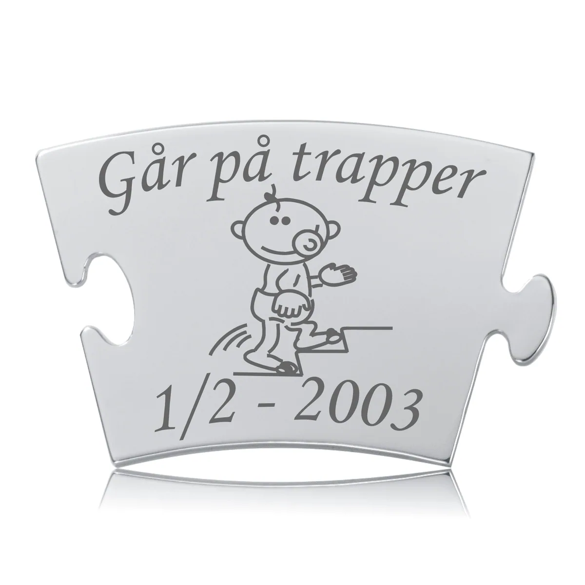 Memozz Classic mindebrik i sølvfarvet rustfrit stål med gravering af teksten "Går på trapper" og en tegning af en glad baby, der klatrer op ad en trappe. Graveringen er mørkegrå.