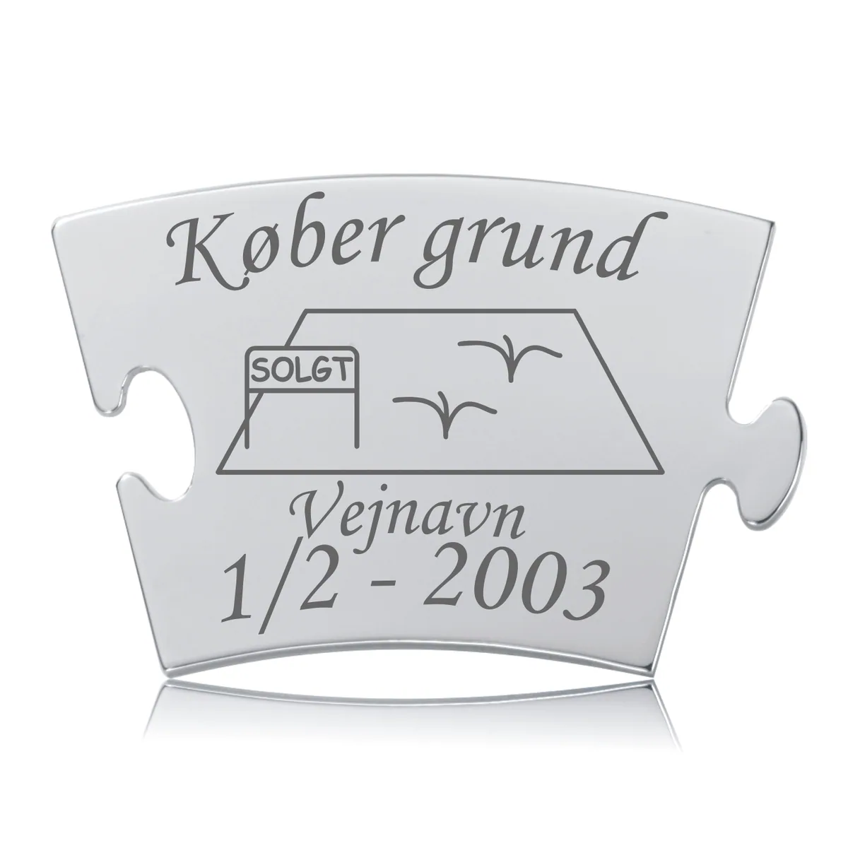 Memozz Classic brik "Køber grund" i håndpoleret rustfrit stål med mørk lasergravering, der viser et hus, "SOLGT" skilt og fugle, samt "Vejnavn" og dato.